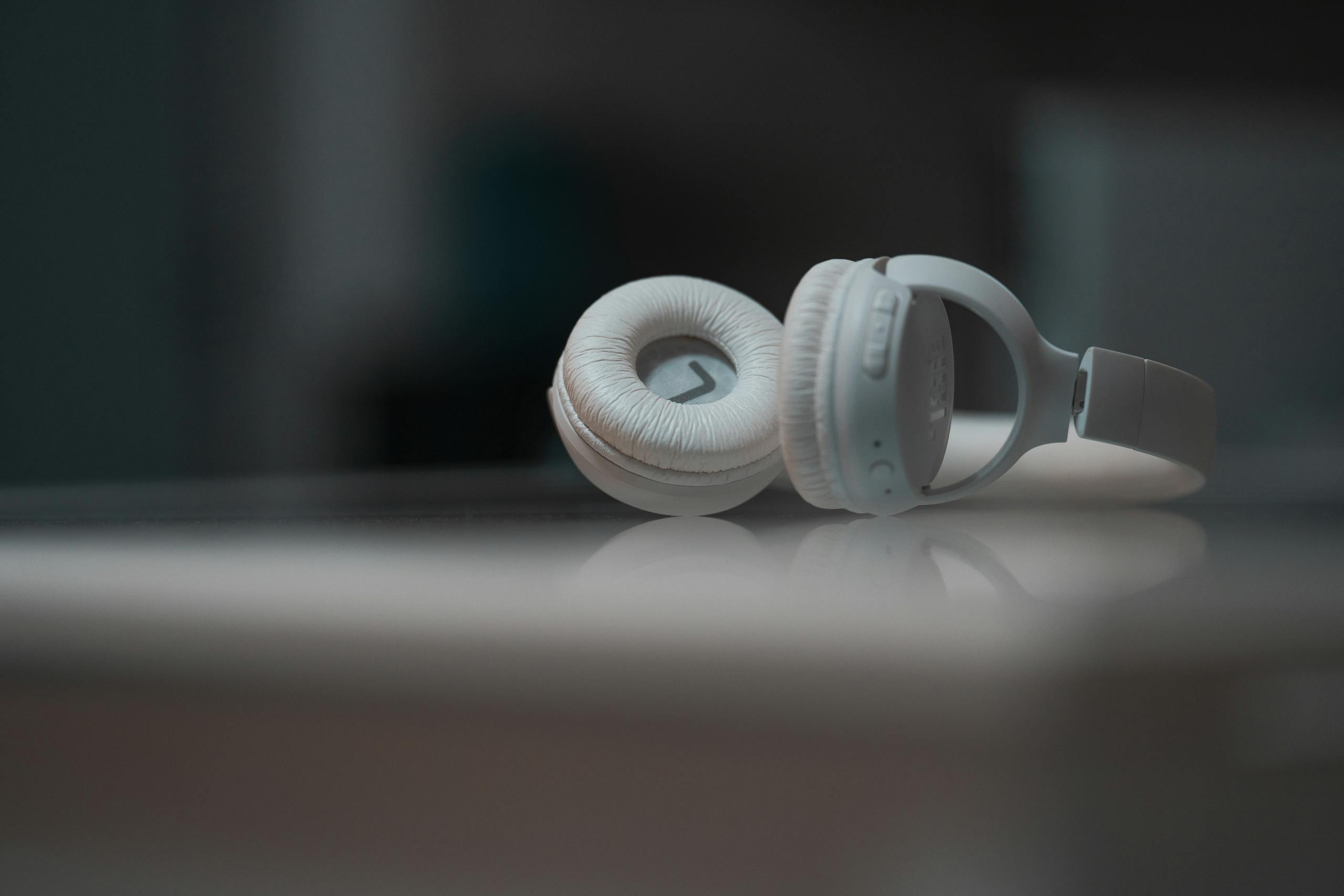 Close-up view of white headphones on a reflective surface, showcasing modern audio technology.