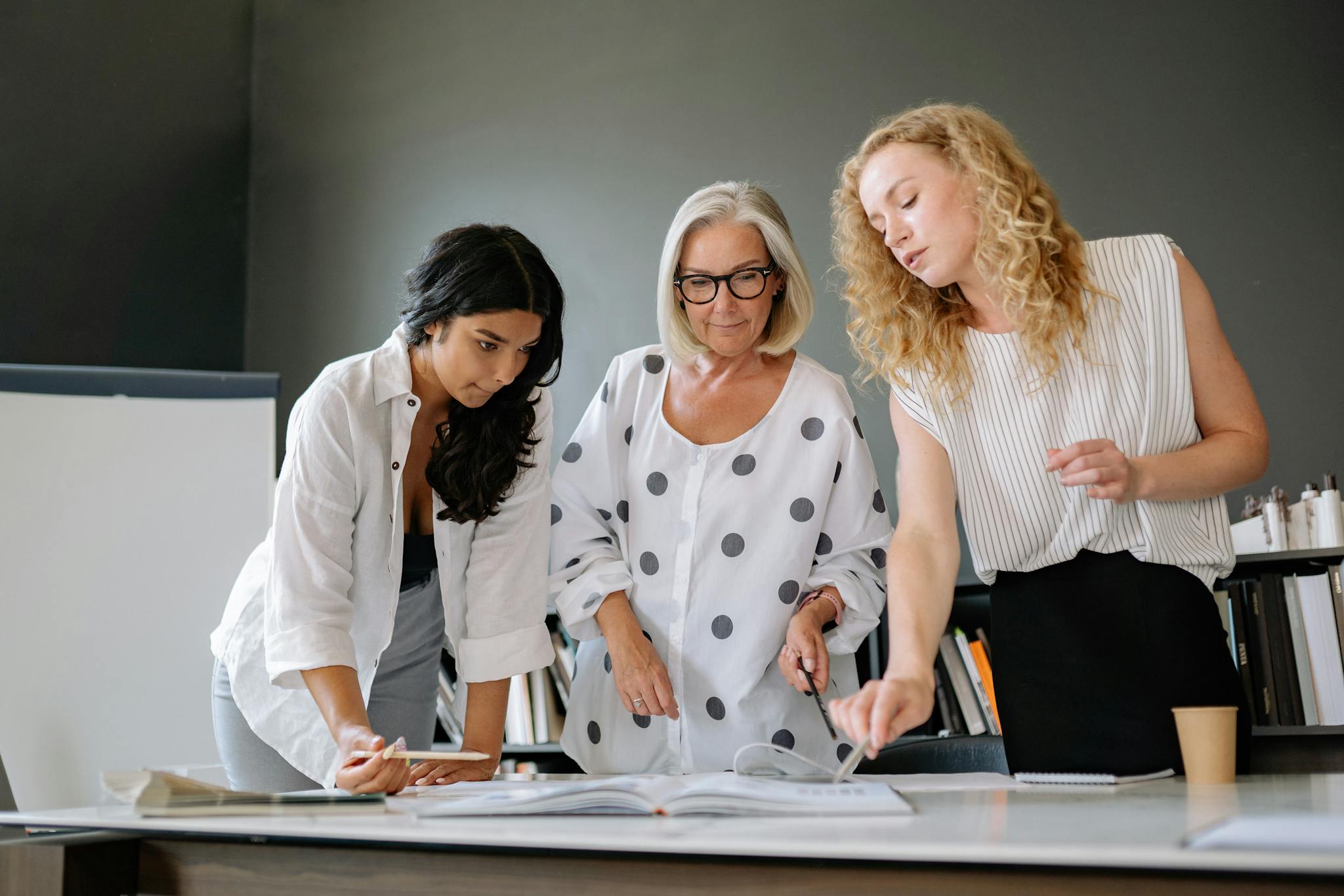 Three professional women collaborating in an office, discussing a document with focus and teamwork.